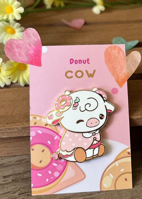Two cute cow-themed pins on cards with decorative elements on a wooden surface.