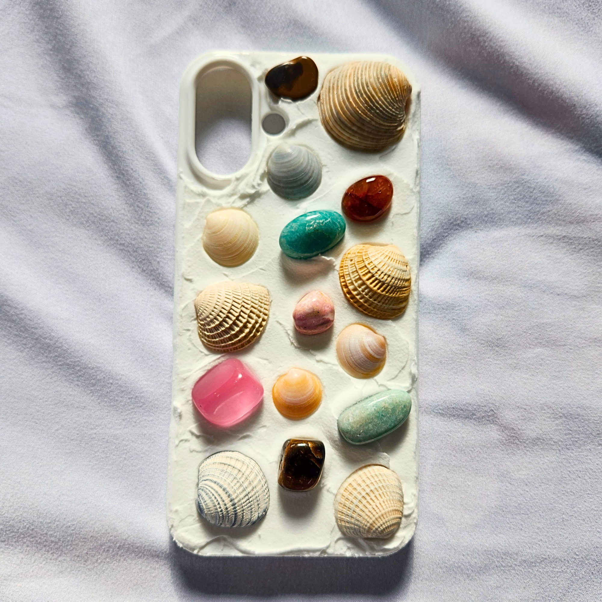 Phone case with colorful shells and stones on a light fabric background