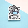 Sticker with a cat holding tissues and text 'Sorry UR ALLERGIC.' on a light blue background