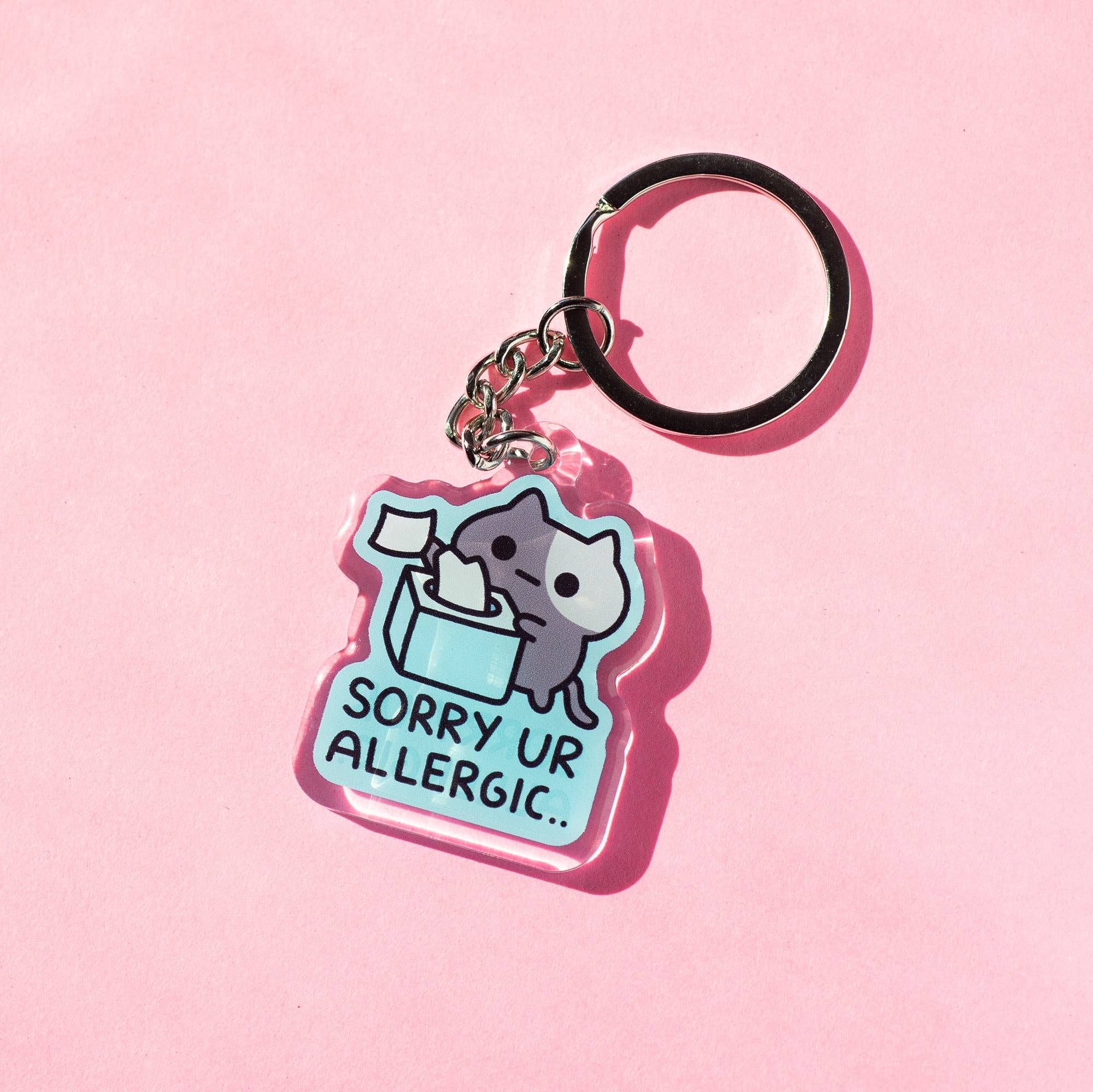 Keychain with a cat design and 'Sorry Ur Allergic' text on a pink background