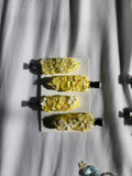 Four yellow and white hair clips with small multicolor sequins, arranged vertically on a white rectangular card over a white fabric background.