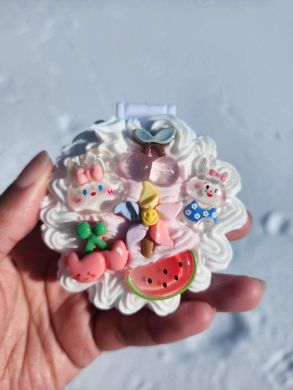 Decorative mirror with cartoon character and colorful elements held by a hand against a light background.