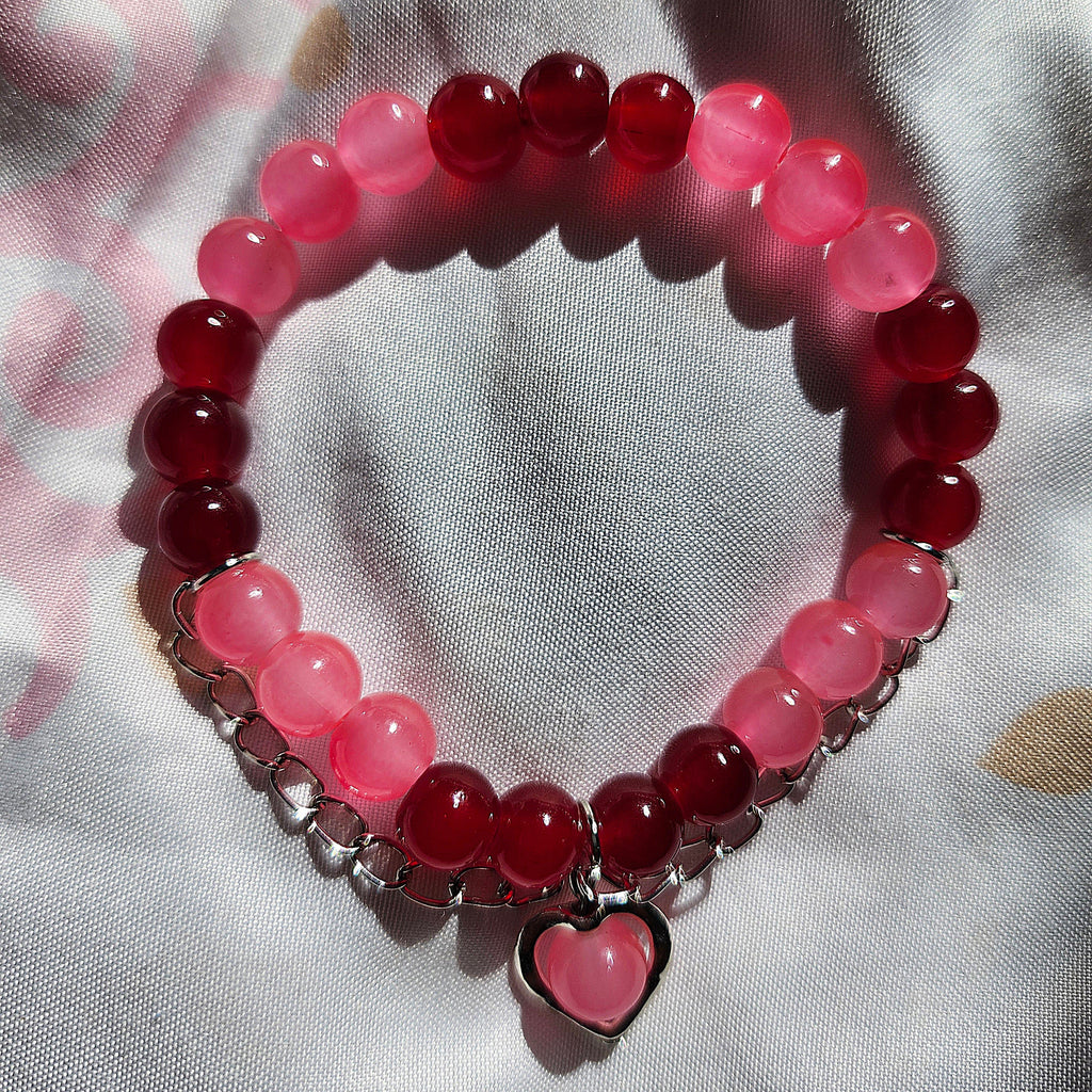 Bracelet with red and pink beads and a heart charm on a light fabric background
