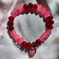Bracelet with red and pink beads and a heart charm on a light fabric background