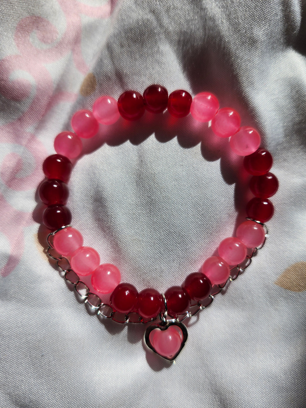 Beaded bracelet with pink and red beads and a heart charm on a light fabric background