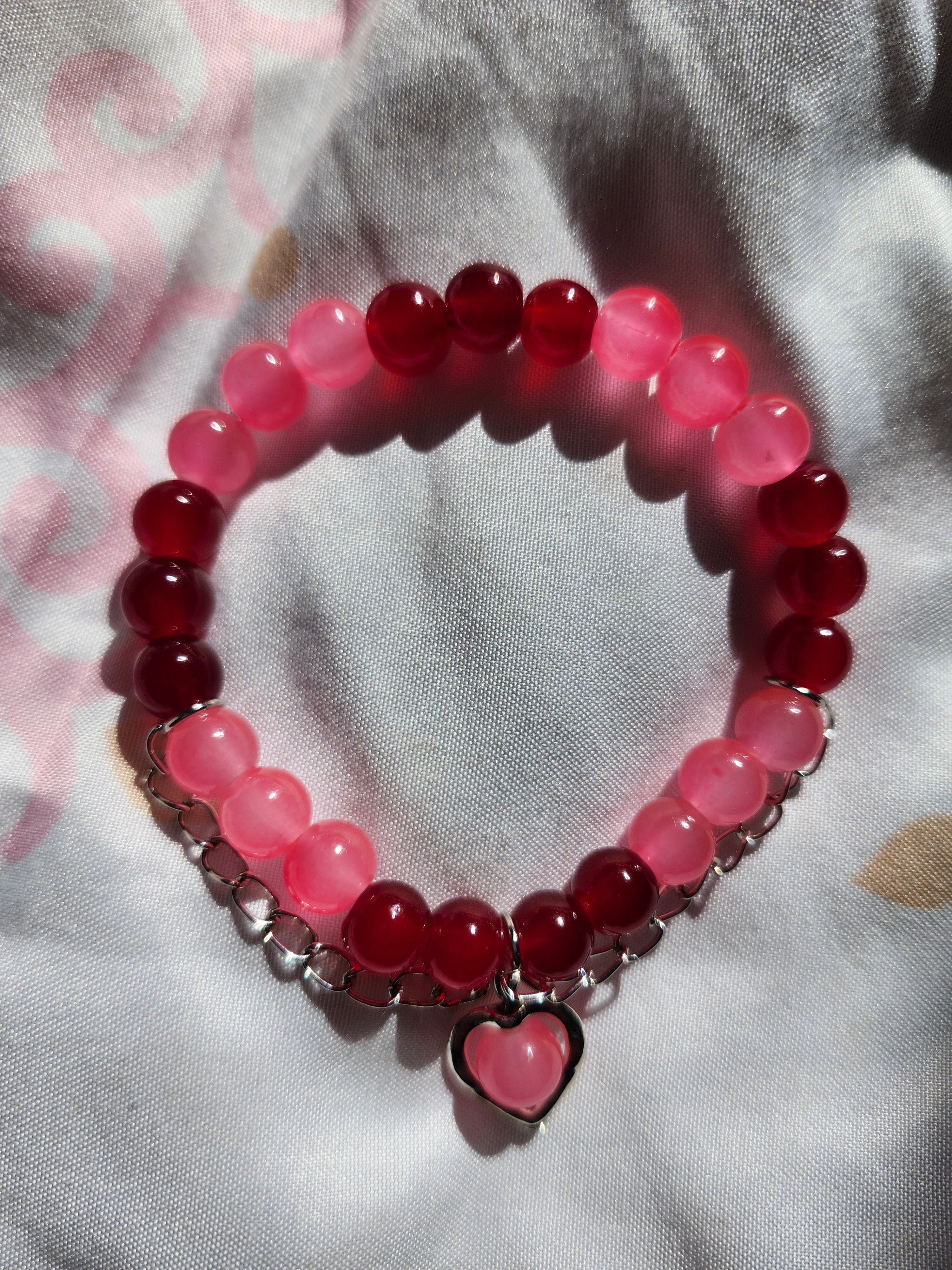 Beaded bracelet with pink and red beads and a heart charm on a light fabric background