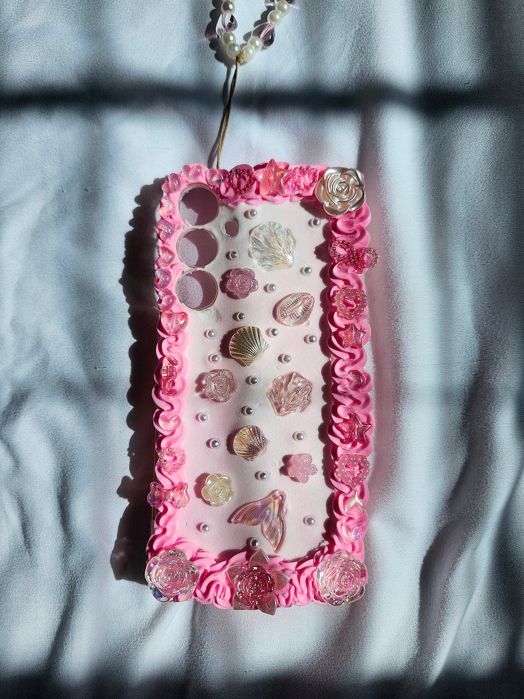 Decorative phone case with pink border and embellishments on a textured surface