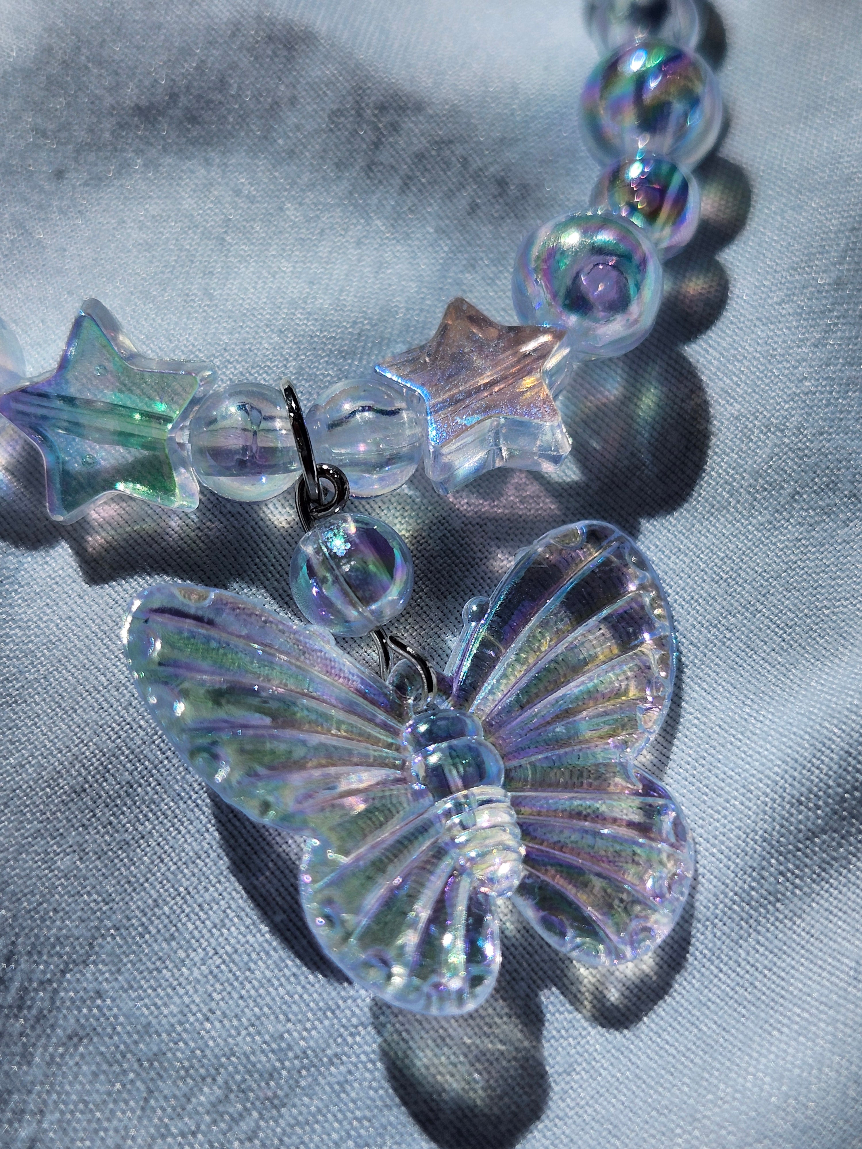 Close-up of a necklace with clear butterfly and star-shaped beads on a textured gray background