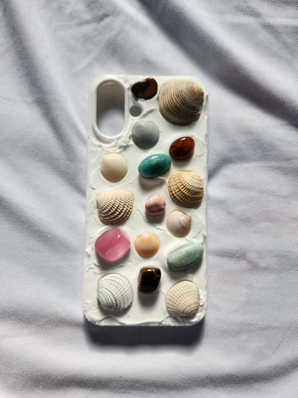 Phone case with various seashells and stones on a white fabric background