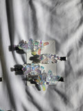 Four butterfly-shaped hair clips with iridescent holographic resin wings and black metal clips, arranged on a white card over a white fabric background.
