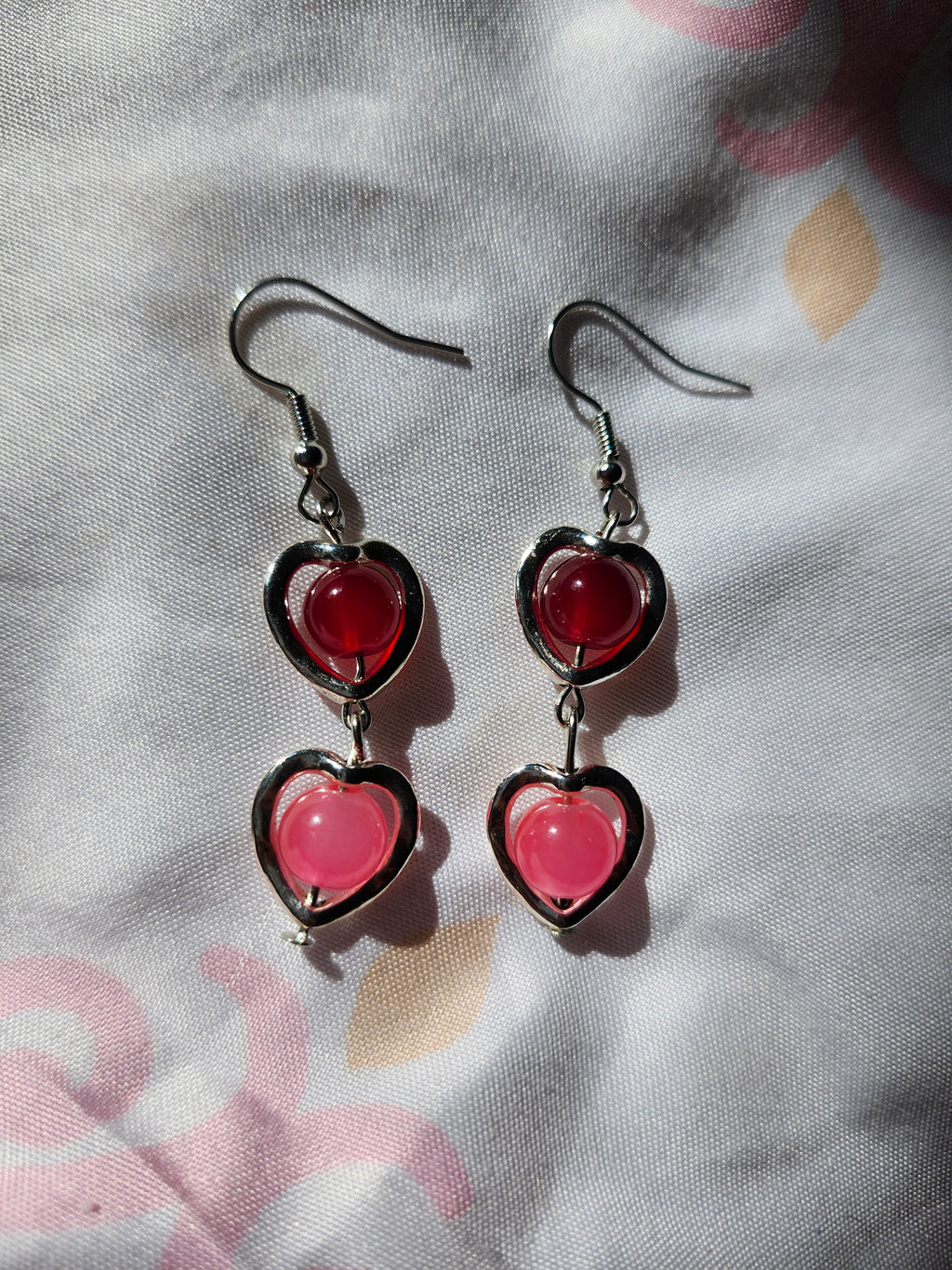 Heart-shaped earrings with red and pink stones on a floral fabric background