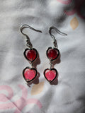 Heart-shaped earrings with red and pink stones on a floral fabric background