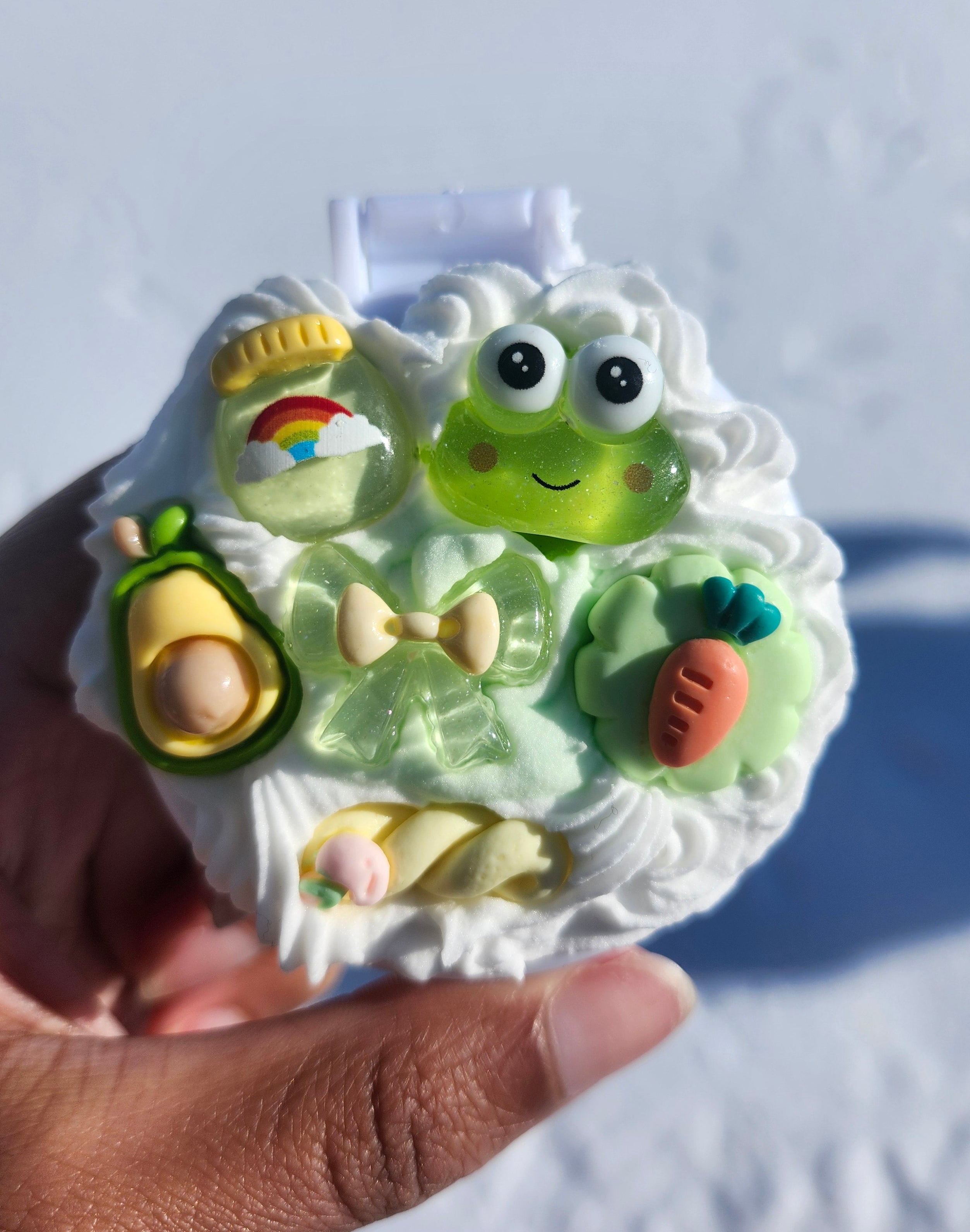 Mirror with green cartoon icing design of a smiling face held by a hand against a light background