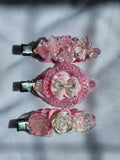 Three decorative hair clips with pink and silver designs on a light gray background
